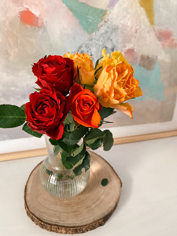 Vase with red, orange and yellow roses in the hall of the house