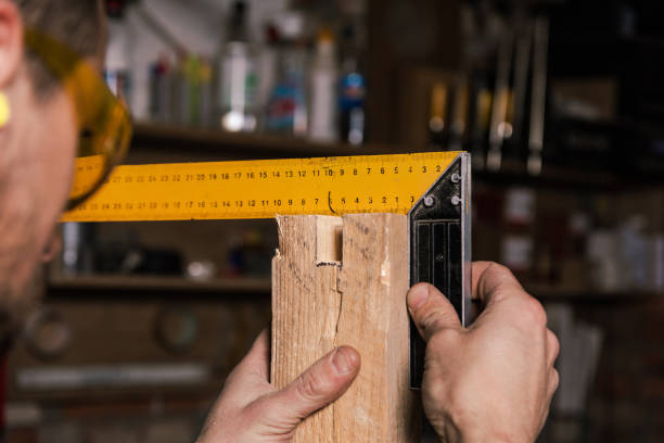 A carpenter works in a furniture workshop with various tools and a board
