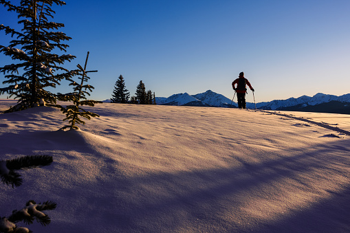 Outdoor Adventure Ski Touring with Scenic Mountain Backdrop - Man recreating on alpine touring skis while skiing high on mountain ridge with scenic views and warm sunset light.