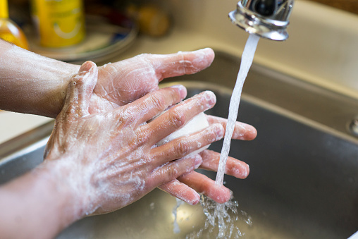Closeup of an anonymous person's hands washing up in the sink with a bar of soap and water from the faucet as they have OCD and wash their hands frequently.