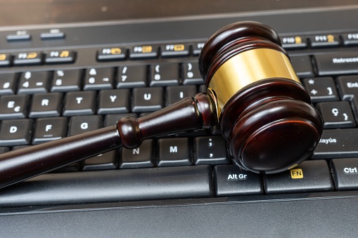 A judge presides over a court, brandishing the mace of justice while a laptop and keyboard display evidence in an ongoing cybercrime case. Technology aids communication between legal professionals.