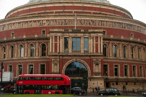 A red bus stops at the facade of Royal Albert Hall as people enter the building in London