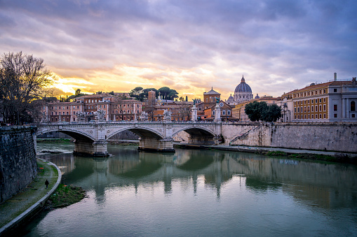 Beautiful bridge over river Tiber and distant view of the dome of the famous St. Peter's basilica during sunset in Rome, Italy