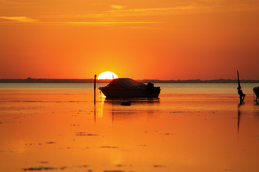 Silhouette of a motor vessel on calm baltic sea during golden sunset. Boat tied to a pole, close to the beach of Greifswald, Germany