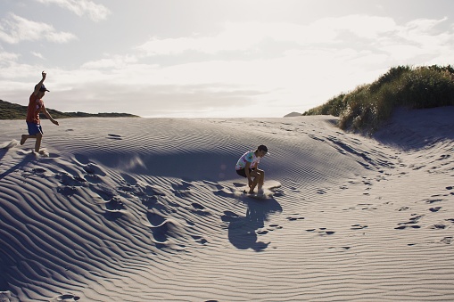 Two boys jump in sand dunes in an evening beach scene landscape.