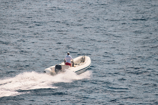 High-angle photo of an unrecognizable man driving a white rigid-hull inflatable boat in the water