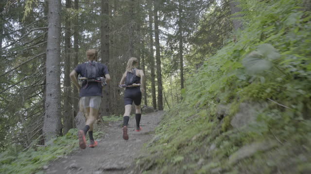 Two trail runners running in a dense forest in the mountains
