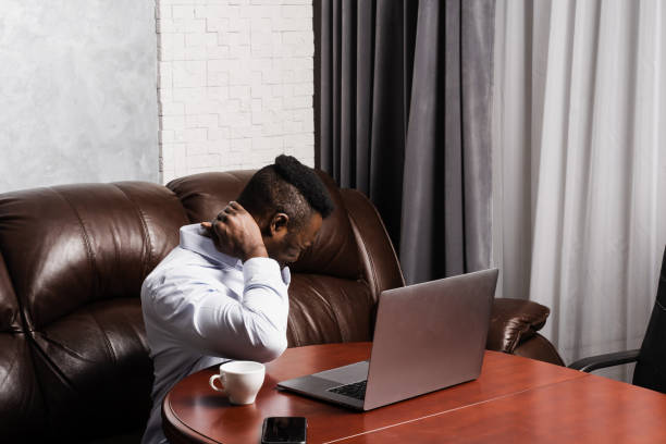 African man with laptop feel neck and spine pain because of spinal nerves compression. Cervical spine osteochondrosis is radicular syndromes after long work at the computer el hombre africano con computadora portátil siente dolor en el cuello y la columna vertebral debido a la compresión de los nervios espinales. la osteocondrosis de la columna cervical es un síndromo radicular después de un largo trabajo en la computador