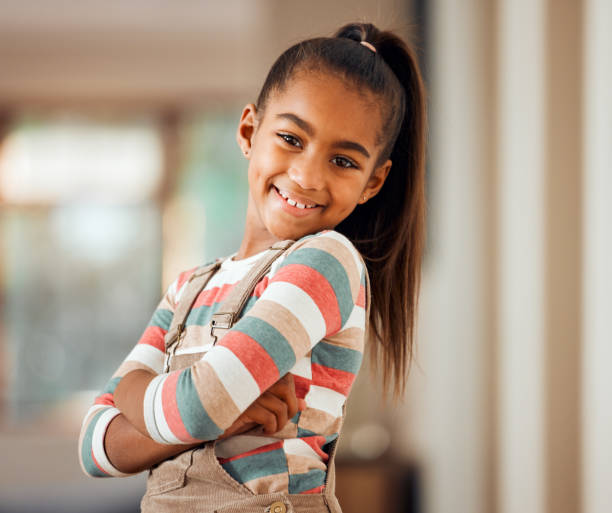 felice, sorriso e ritratto di una bambina nella sua casa con una mentalità positiva in piedi con le braccia incrociate. felicità. bambino bello e giovane con un vestito casual, elegante e alla moda in posa in casa. - child student adolescence cute foto e immagini stock