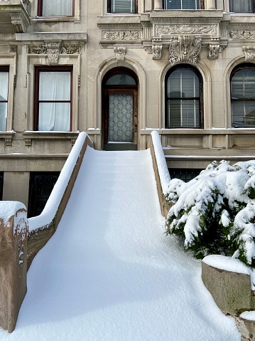 Long, tall stoop of a stone townhouse in Harlem, New York City, covered in a layer of thick, smooth snow the day after a winter storm