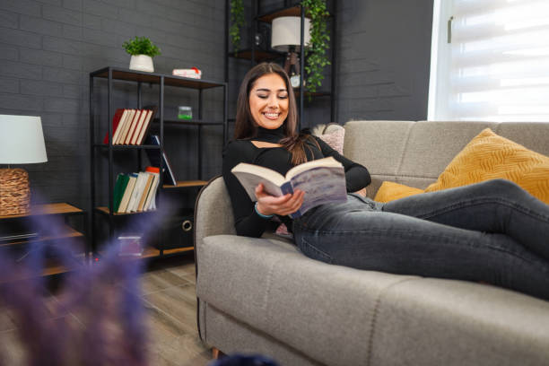 istock Smiling young woman is relaxing on the couch reading 1474689111