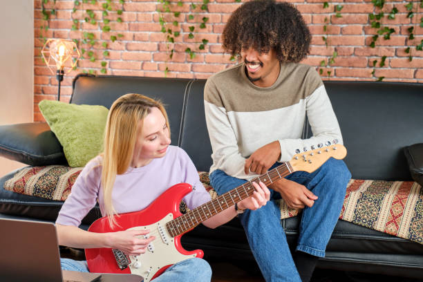 istock multiracial couple learning to play the guitar with tutorials on the sofa at home 1474694839