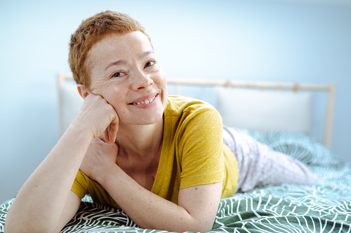 Short hair woman in yellow t-shirt looking at camera while relaxing on bed