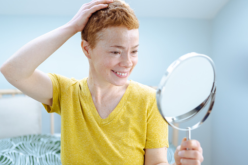 Short hair woman in yellow t-shirt holding mirror while relaxing at home