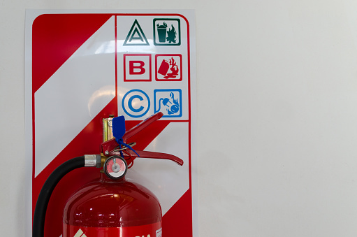Fire extinguisher hanging on the white wall with instructions. Safety and security concept, copy space.