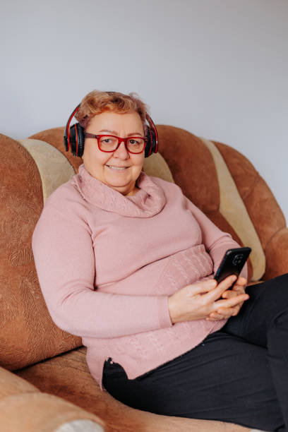 なだめるような音太りすぎの年配の女性がヘッドフォンでソファでリラックスしている - senior women cheerful overweight smiling ストックフォトと画像