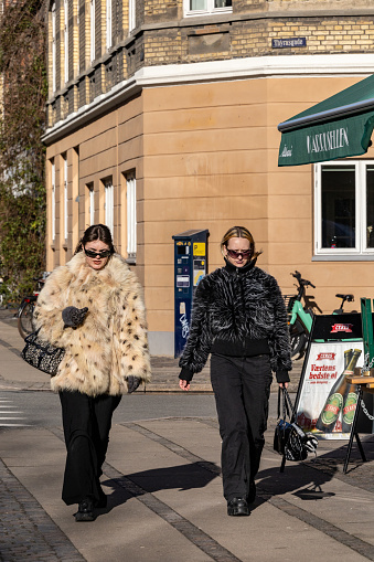 Copenhagen, Denmark March 15, 2023 Two fashionable young women with fake fur coats and sunglasses  walk down the street in Norrebro.