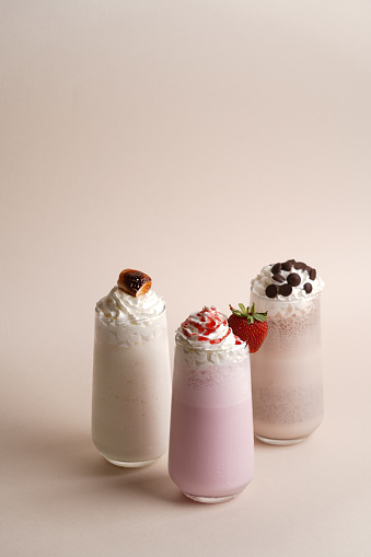 Set of milkshake with whipped cream on pink background. Milk smoothies cocktails with fresh strawberry, chocolate and marshmallow