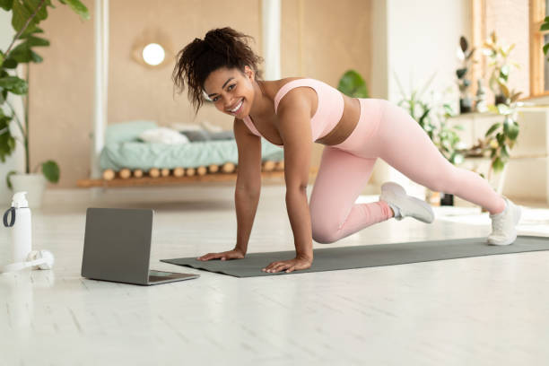 istock Domestic training concept. Black lady doing cross body mountain climbers exercise, watching online tutorial on laptop 1474723450