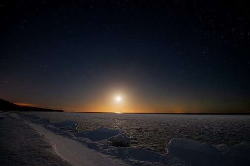 Seashore covered with ice under a starry sky with moonset.