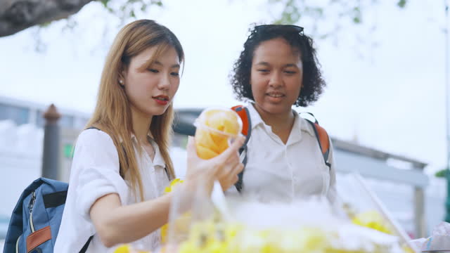 Young tourist Korean tourist buying mango on street fruit cart in tourist market Bangkok ,Thailand.