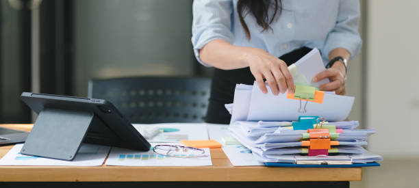 una mujer de negocios está revisando pilas de archivos y carpetas en papel que contienen documentos incompletos y completados. - empleado de archivo fotografías e imágenes de stock