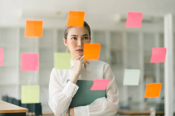 In a creative office, a startup young and confident businesswoman is strategizing using sticky notes.