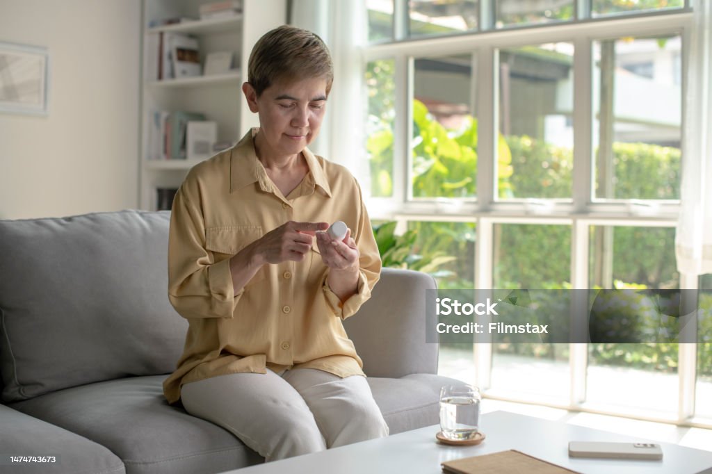 Mature woman read medicine instruction on packaging. Happy mature Asian woman hold bottle with pills read medicine instruction on packaging. Nutritional Supplement Stock Photo