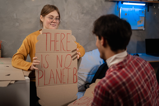 Student activists prepare banner protesting over pollution and global warming sitting in dormitory. Silent protest to save planet earth. Woman showing a banner of There is no Planet B. Copy space