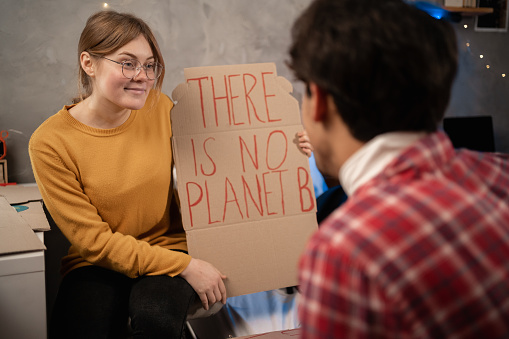 Students prepare banner protesting over pollution and global warming sitting in dormitory. Protest to save planet earth. Woman showing a banner of There is no Planet B for her boyfriend. Close up