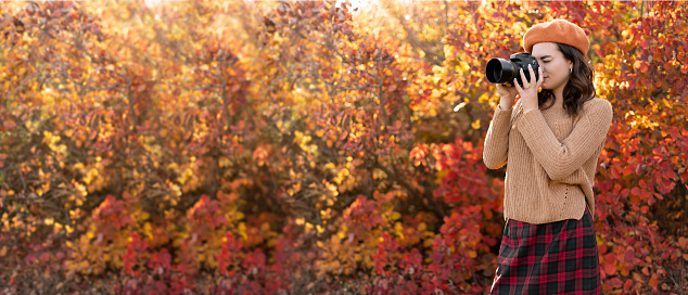 Portrait of a photographer photographing in autumn park with orange foliage covering her face with the camera. Copy space. Banner