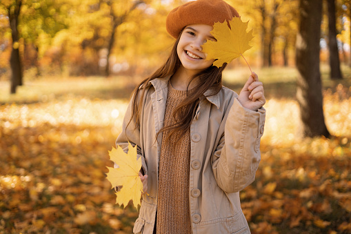 Excited happy fall girl smiling joyful holding autumn leaves outside in colorful fall forest. Autumn portrait of teen girl with yellow maple leaves. Copy space
