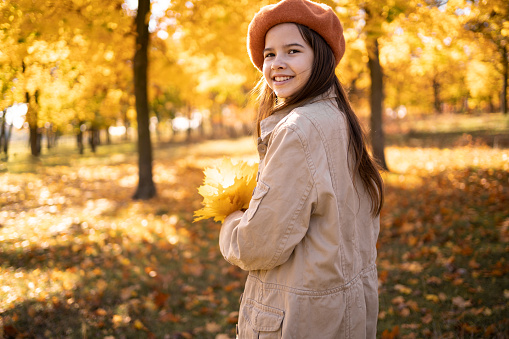 Student girl wearing coat and hat in autumn park. Beautiful autumn teen lady with autumn leaves on fall nature background. copy space