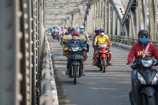 Hue, Vietnam - march 12, 2020 : Automobile and pedestrian steel bridge over the river in Hue town, Vietnam. People on motorbikes on the road across the bridge
