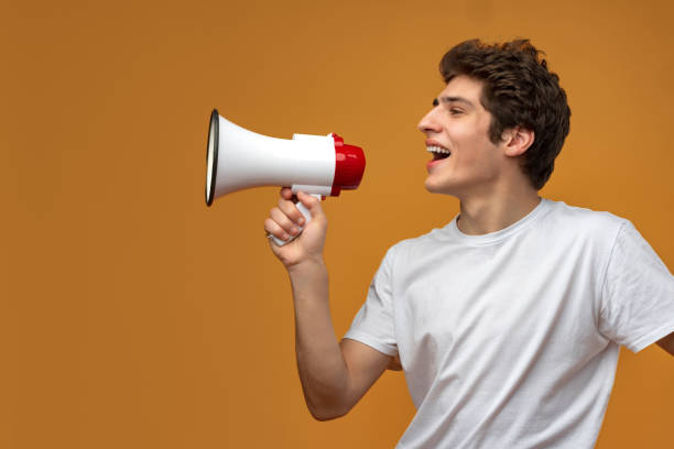 istock Young man shouting into megaphone making announcement against yellow background 1474756247