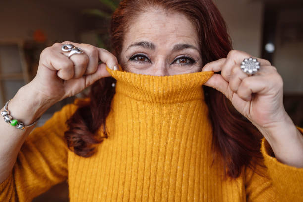 mature woman cover her mouth with sweater, happy smiling. portrait of senior woman at home in winter wearing a nice yellow sweater. mature woman cover her mouth with sweater, happy smiling. portrait of senior woman at home in winter wearing a nice yellow sweater. hair covering eyes stock pictures, royalty-free photos & images