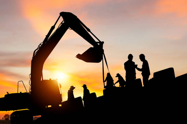 istock Silhouette of Engineer and worker checking project at building site, Engineer and builders in hardhats discussing on infrastructure construction site sunset in evening time background 1474762556
