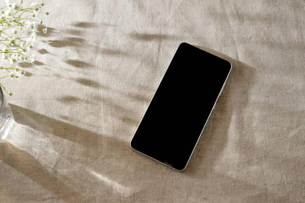 istock Mobile phone on beige table background with floral sunlight shadows, Aestethic minimalist bohemian branding or business template, copy space 1474764988