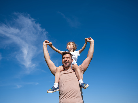 Portrait of happy man holding his little daughter on neck while having rest on summer day