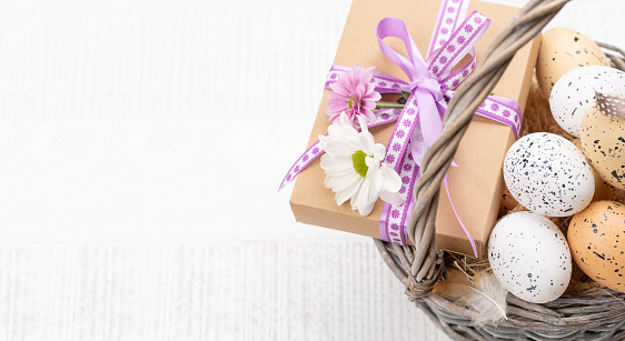 Gift box with flowers and Easter eggs basket on a wooden background with space for your greetings