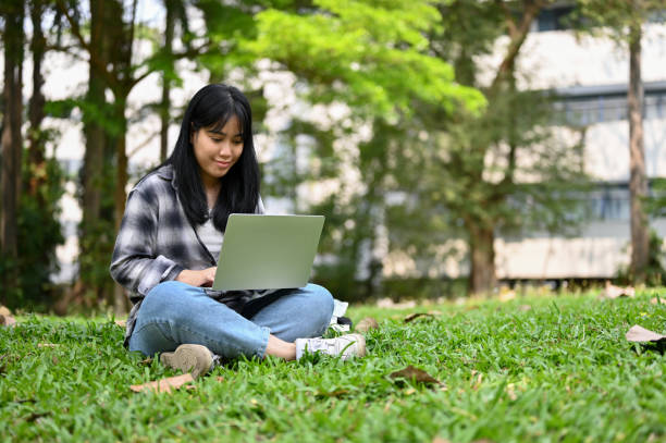istock Charming young Asian female college student using laptop in the campus park. 1474767827