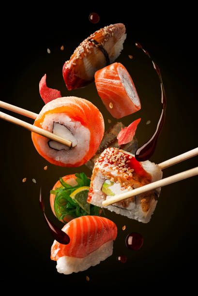 involtini di sushi in assortimento in onda. concetto di levitazione. sfondo nero. - sushi foto e immagini stock