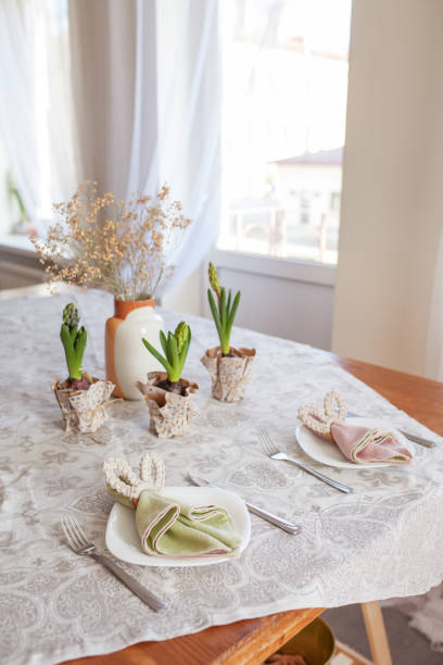 Spring festive dining table setting with flowers, napkins and cute bunny decor on linen tablecloth. Easter time. Cozy home