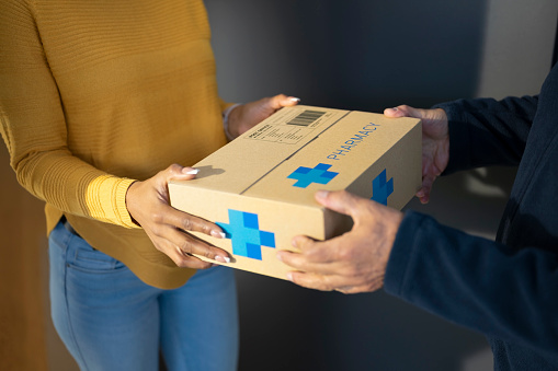 Woman receiving medicine box from delivery person.