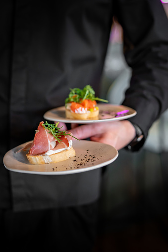 waiter hand hold plate Bruschetta with prosciutto and cream cheese