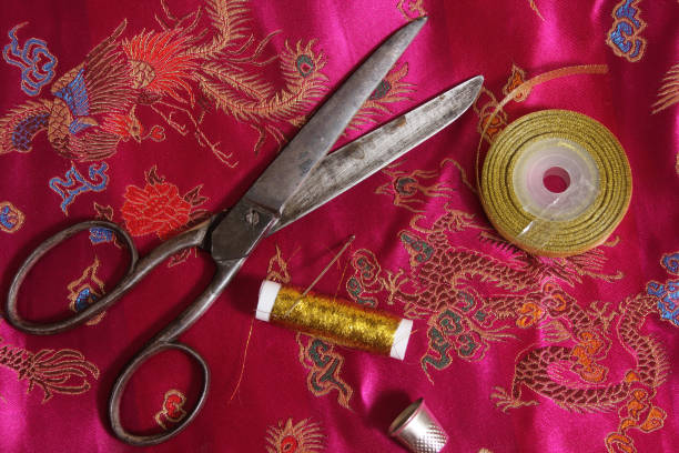 istock Spool of Gold Thread and Thimble on Vintage Asian Pink Silk Fabric 1474780214