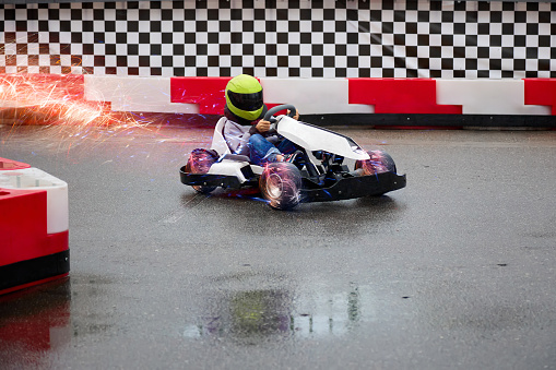 Child driving a real go-kart on a children's race track carefully bypasses an obstacle. Young karting racer trains at the circuit on wet asphalt after the rain