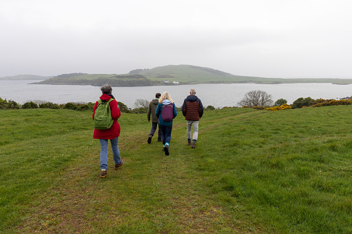 Senior friends on a hiking staycation in Dumfries and Galloway, Scotland. They are walking through a grassy rural area with a lake in the background.