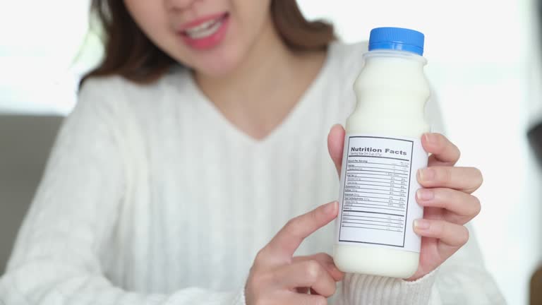 Close up of woman nutritionist hand showing and giving advice about nutrition fact label on dairy product bottle, Producing a vlog, live broadcast streaming for healthy food