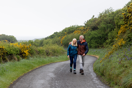 Senior couple walking along a road together while on a hiking staycation in Dumfries and Galloway, Scotland.